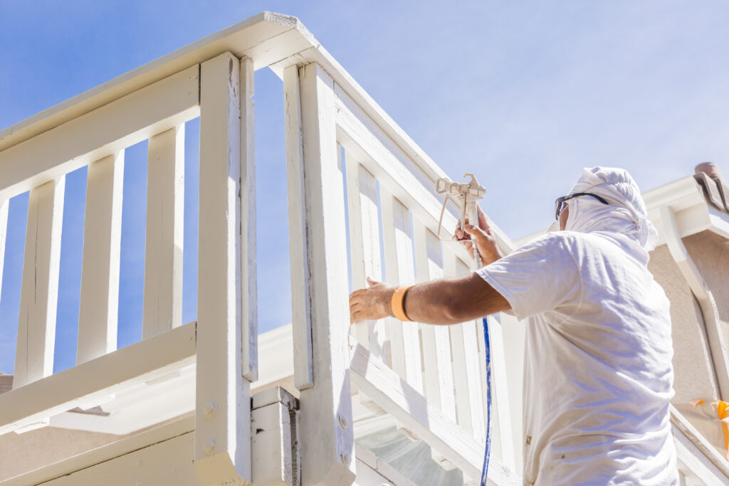 House Painter Wearing Facial Protection Spray Painting A Deck of A Home.